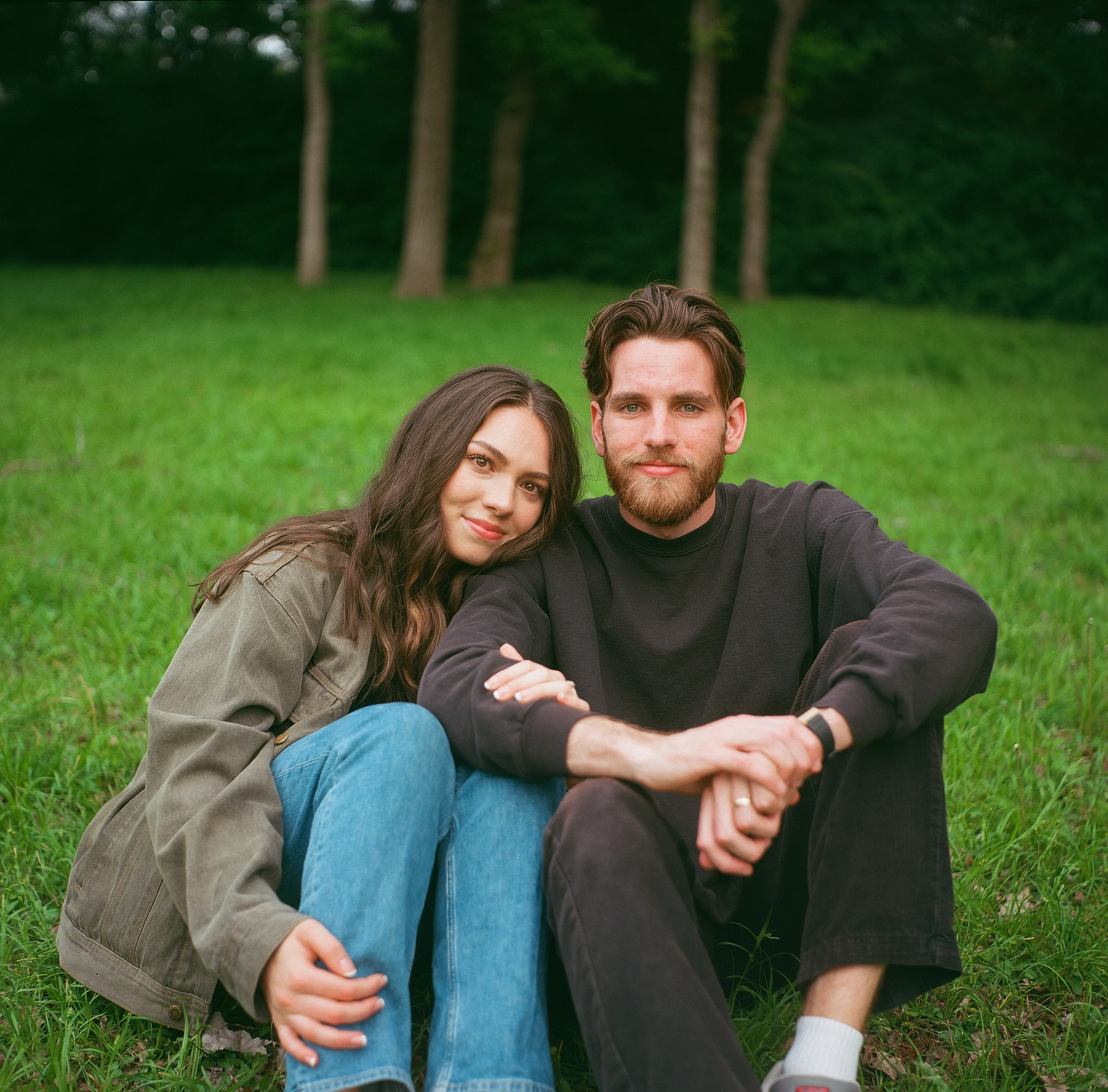 Libby and Dawson sitting on the grass at White Rock Lake, with Libby cuddling up to Dawson’s shoulder during their couples session in Dallas, Texas.