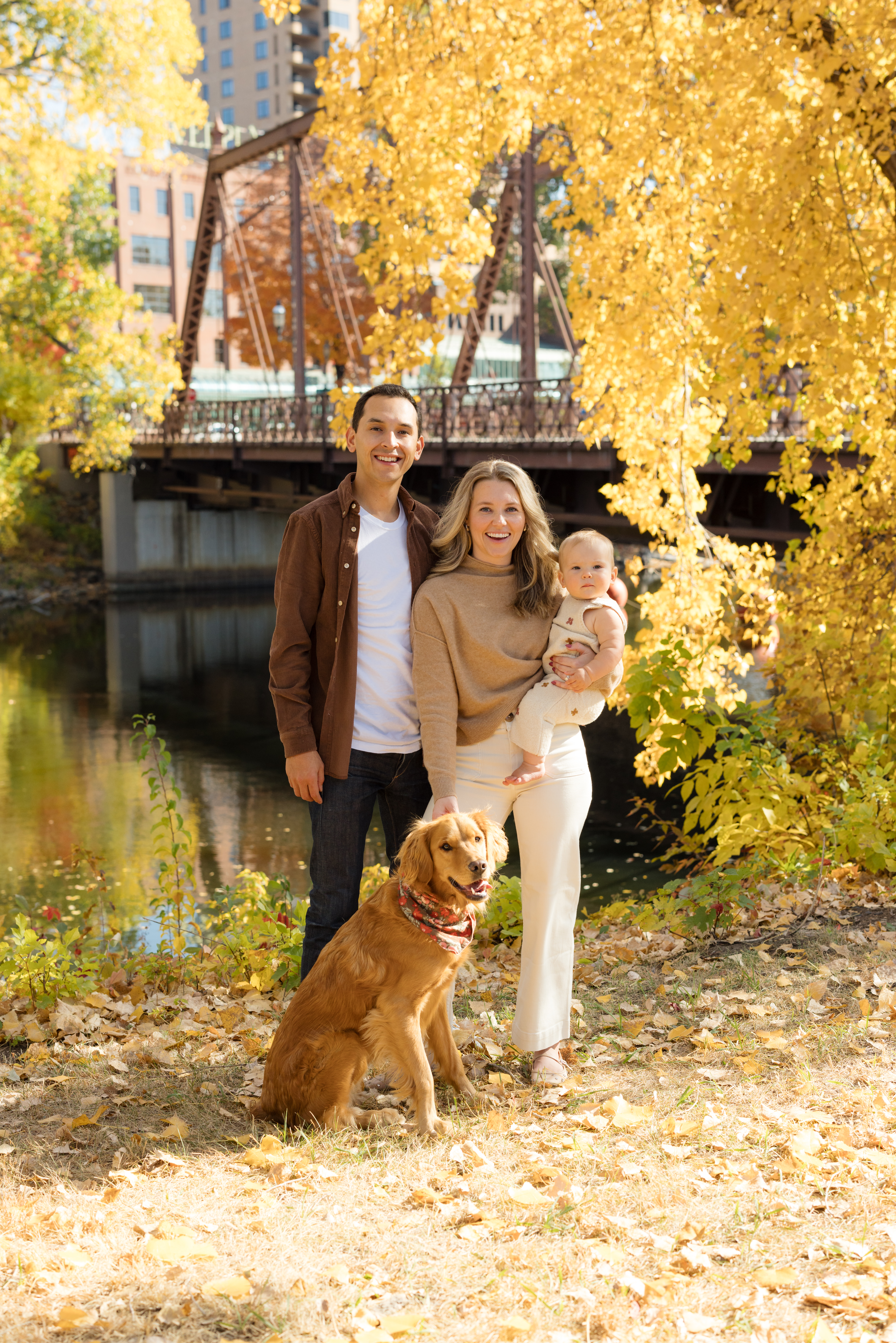 The Chapple family—Tony, Storm, Lily, and their golden retriever, Scout—posing in front of vibrant fall foliage at Nicollet Island Pavilion in Minnesota.