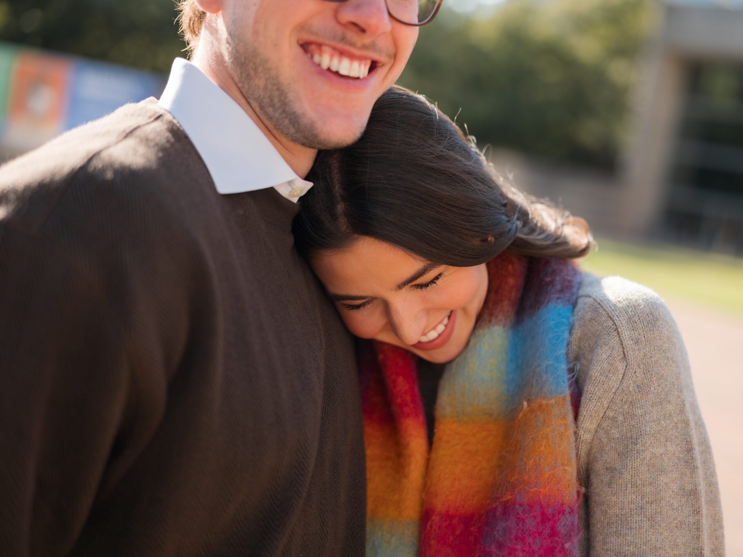 Close-up engagement photo of Campbell and Charles in downtown Dallas, smiling joyfully as she cuddles into his chest, capturing a warm and intimate moment.